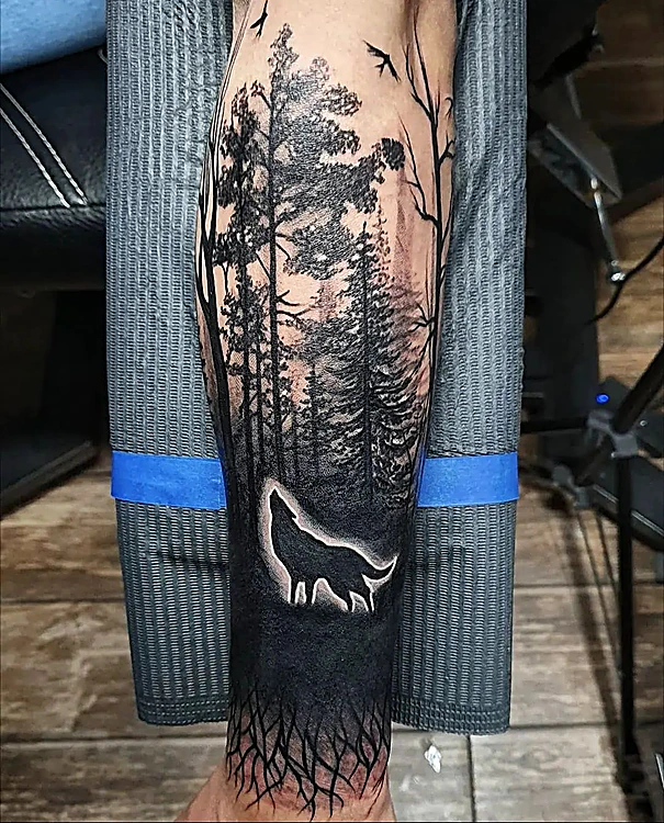 Bosque de pinos en negro sólido con un lobo aullando en silueta blanca, en el antebrazo